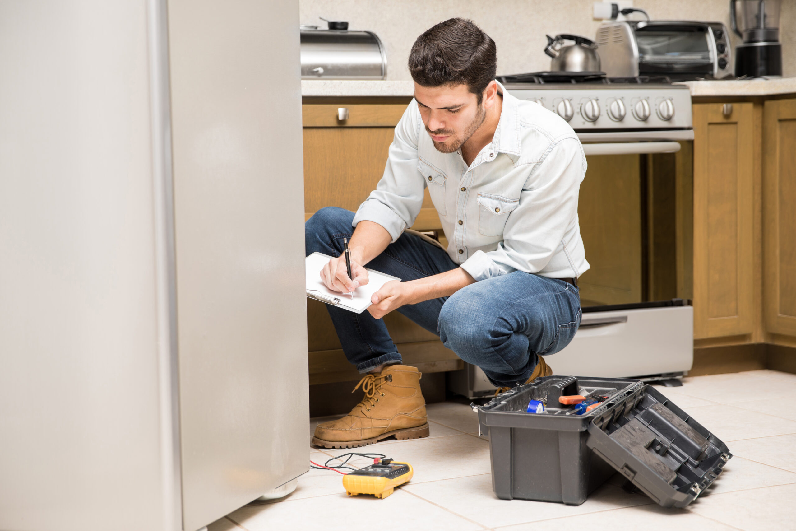 Portrait of a handsome male technician doing a work report on a broken fridge in a home kitchen